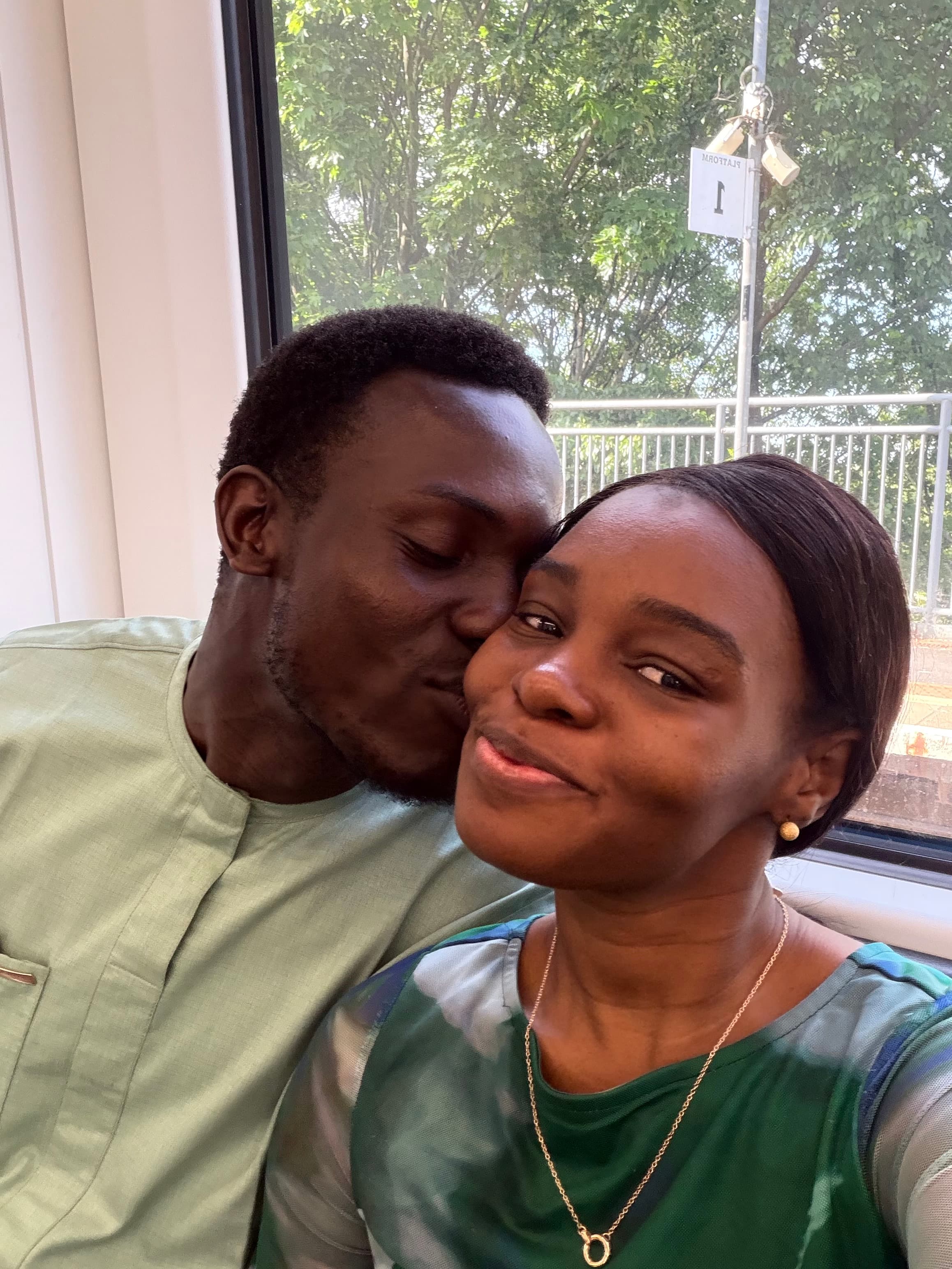 Ayo kissing Ola's cheek by a window